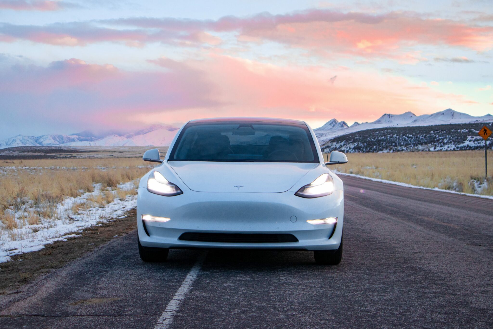 picture of tesla on a road with mountains in the background and a pink sky