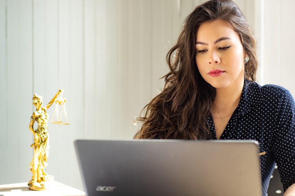 a woman working on her computer with a statue of Lady Justice next to her 